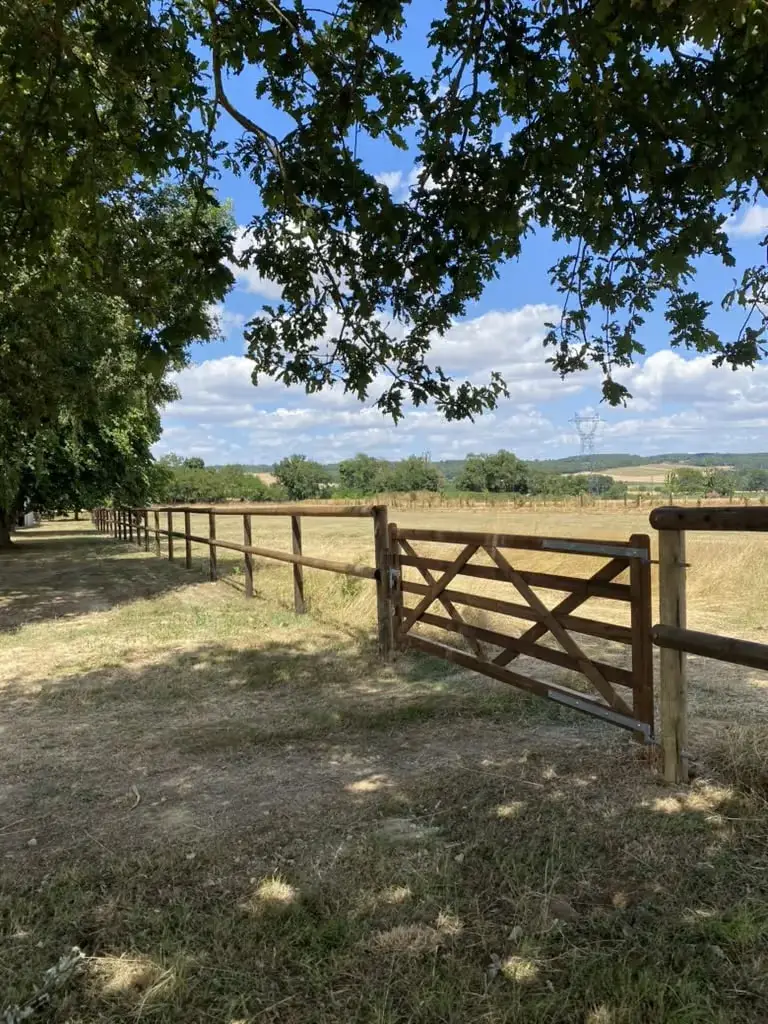 Clôture bois à lices avec portail en chêne à l’entrée d’un pré