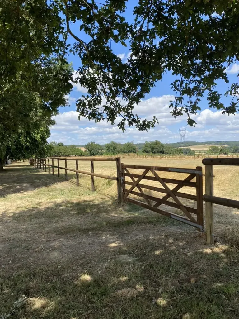 Clôture bois à lices avec portail en chêne à l’entrée d’un pré